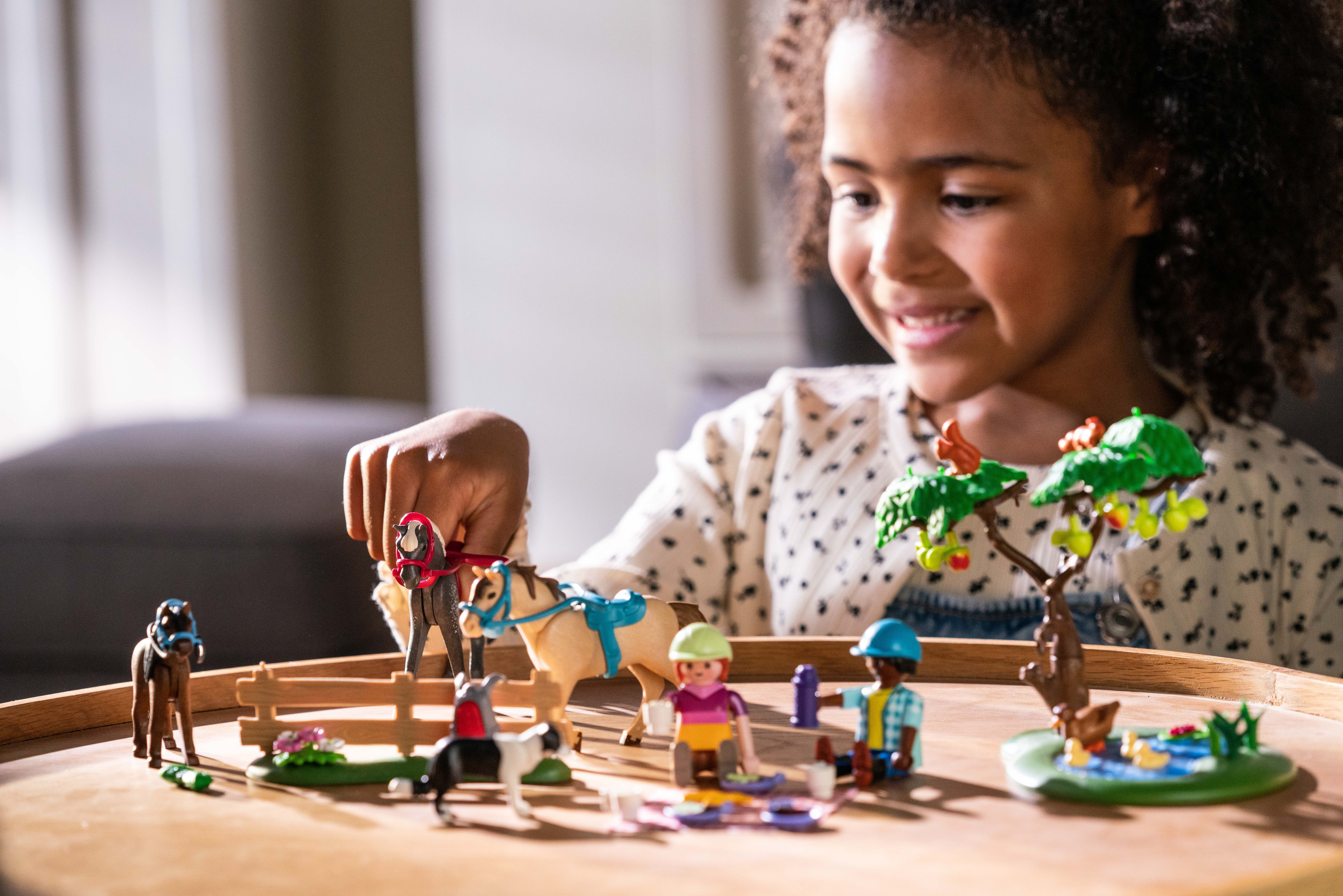 Mädchen spielt mit Playmobil Reiterhof Figuren. 